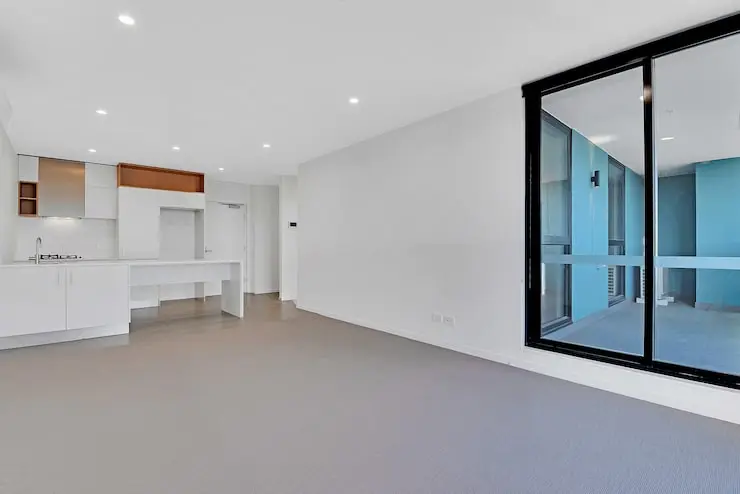 Modern minimalist apartment interior with white walls, recessed lighting, and large glass sliding doors leading to a balcony.