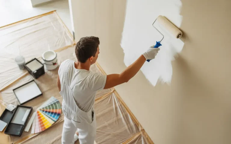 Professional painter applying white paint with roller showing how much does it cost to paint a room with supplies and color swatches visible.