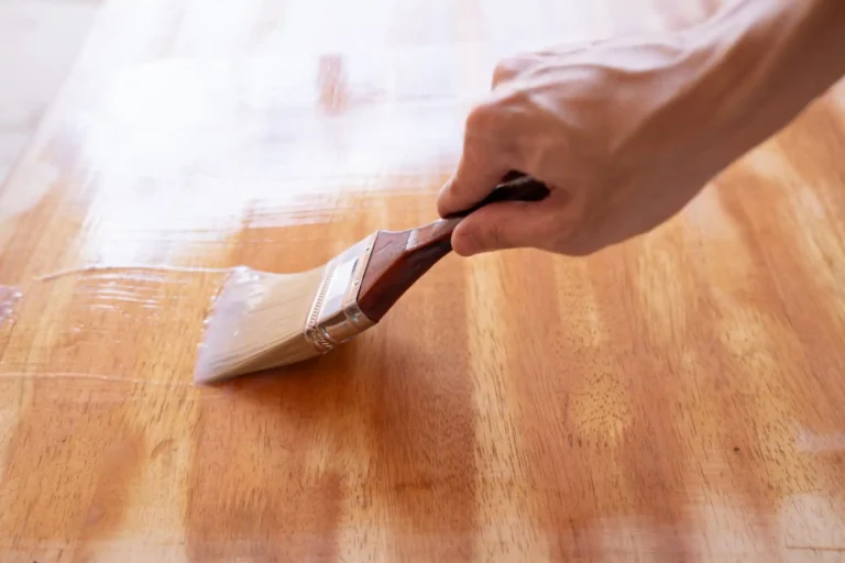 Applying oil-based polyurethane wood finish with a natural bristle brush on a hardwood floor surface for a durable protective coating