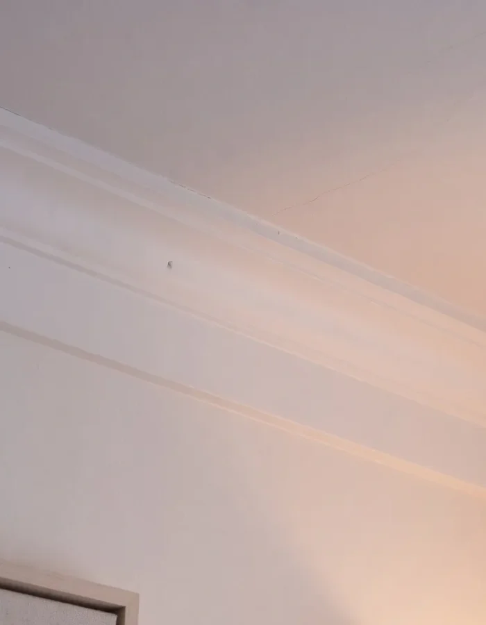 A close-up of simple bed molding trim meeting at a bedroom ceiling corner, showing its low-profile, understated detail.