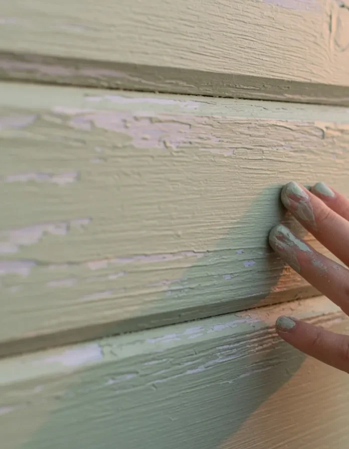 Touching painted siding to check if it's dry to the touch, the first step before recoating or letting the paint fully cure.