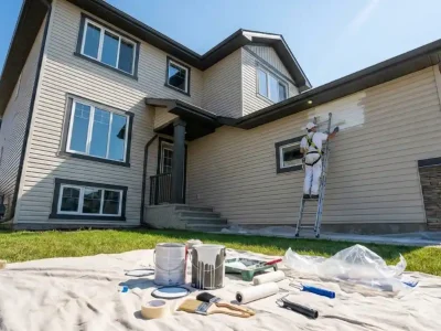 Professional painter on ladder demonstrating exterior house painting cost factors including labor and home size on modern two-story home