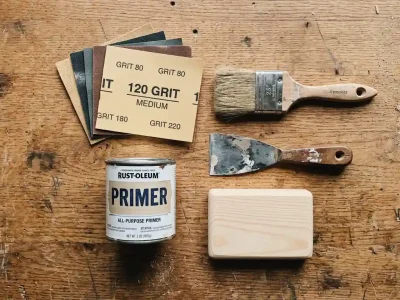 Sandpaper grits, Rust-Oleum primer, paintbrush, and putty knife laid out for how to prepare wood for painting