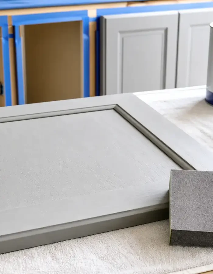 A cabinet door prepared for painting with sanding tools, paint supplies, and a clean, protected work surface.